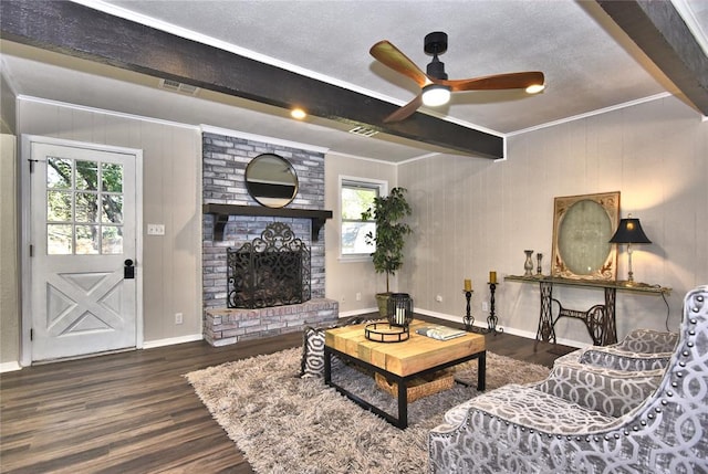 living room with a brick fireplace, ceiling fan, crown molding, wood-type flooring, and beamed ceiling