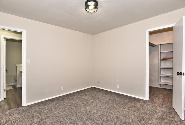 unfurnished bedroom with a walk in closet, a closet, and dark carpet