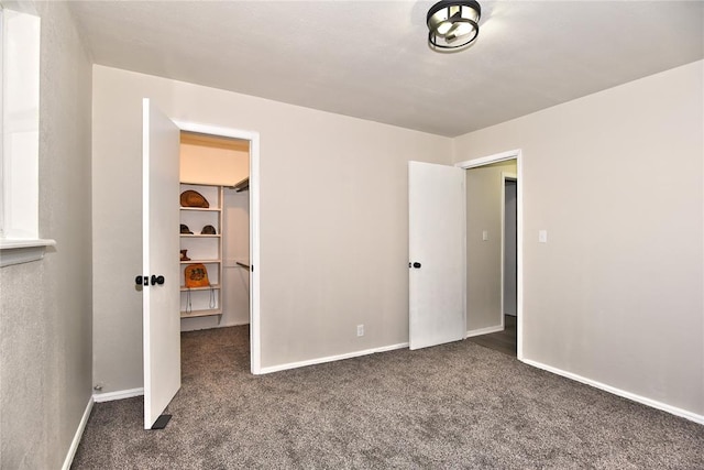 unfurnished bedroom with a walk in closet, dark carpet, and a closet