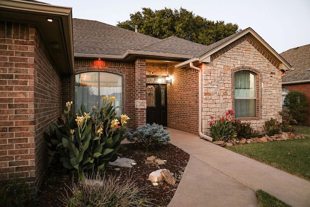 doorway to property with brick siding and roof with shingles