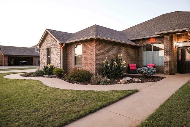 view of property exterior featuring stone siding, brick siding, a shingled roof, and a yard