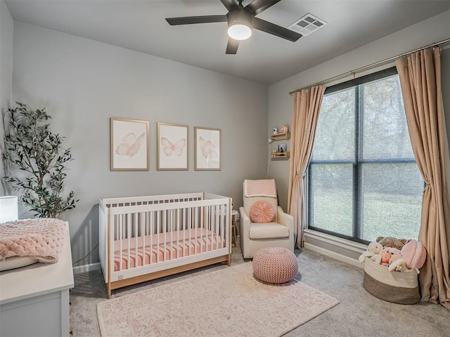 bedroom featuring multiple windows, ceiling fan, light colored carpet, and a nursery area