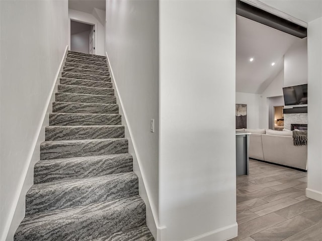 stairway with high vaulted ceiling and a stone fireplace