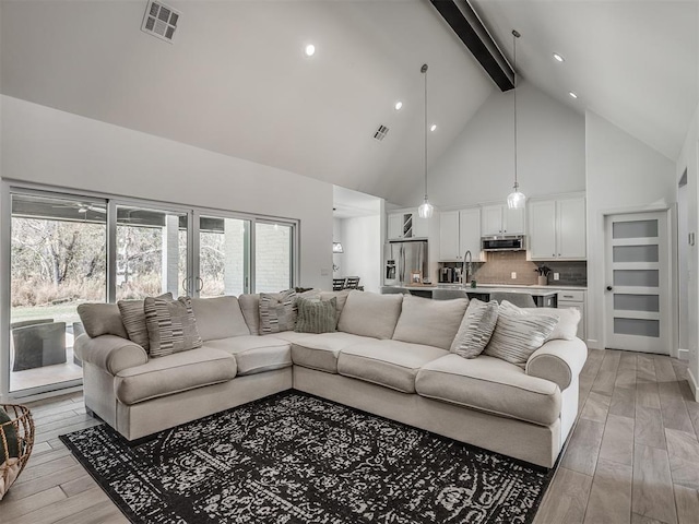 living room with sink, light hardwood / wood-style flooring, beamed ceiling, and high vaulted ceiling