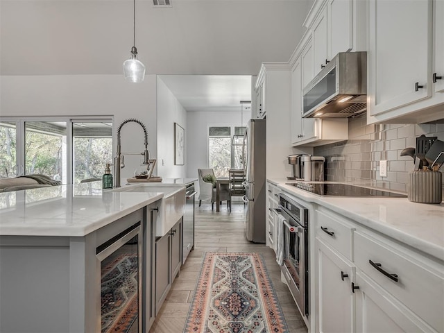 kitchen featuring light wood-type flooring, stainless steel appliances, pendant lighting, white cabinets, and wine cooler