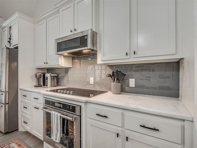 kitchen featuring light stone countertops, light wood-type flooring, backsplash, stainless steel appliances, and white cabinetry