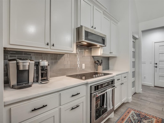 kitchen with white cabinets, light wood-type flooring, stainless steel appliances, and backsplash