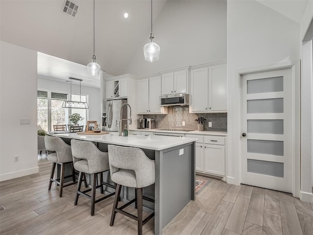 kitchen with hanging light fixtures, appliances with stainless steel finishes, white cabinets, and a center island with sink