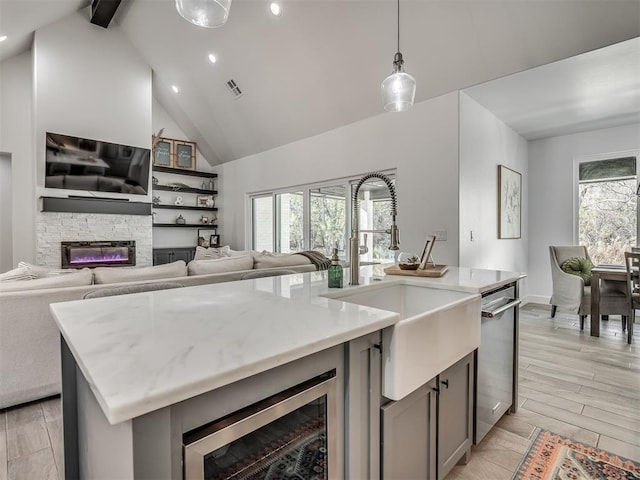 kitchen with dishwasher, hanging light fixtures, a wealth of natural light, a center island with sink, and a stone fireplace