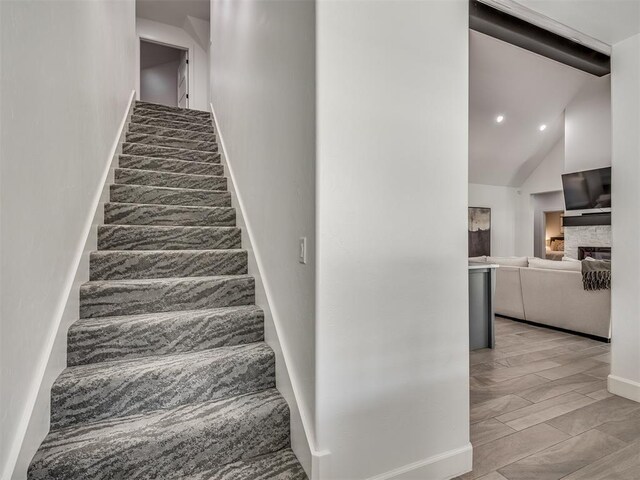 stairway featuring wood-type flooring, a stone fireplace, and lofted ceiling