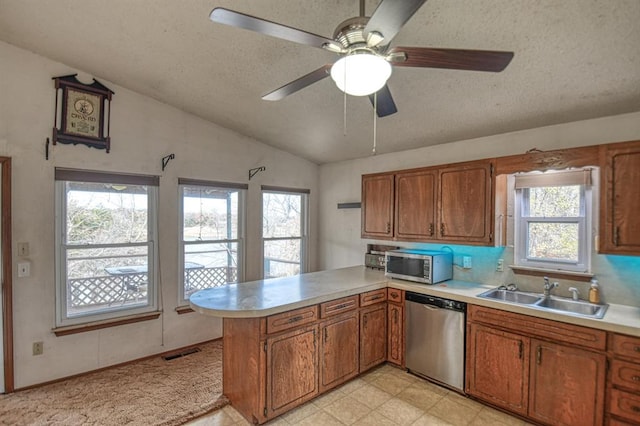 kitchen with kitchen peninsula, appliances with stainless steel finishes, a textured ceiling, vaulted ceiling, and sink