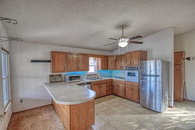 21351 E Tenth St, Hinton, OK 73047 - kitchen featuring stainless steel appliances, a peninsula, brown cabinetry, vaulted ceiling, and light countertops