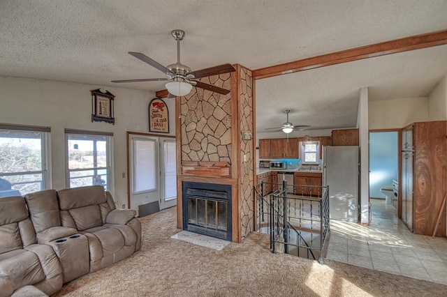 living room featuring light carpet, a textured ceiling, a stone fireplace, and ceiling fan