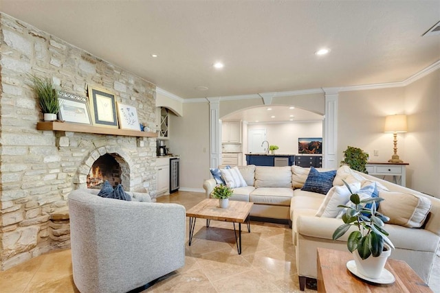 living room with decorative columns, crown molding, sink, a fireplace, and wine cooler