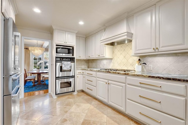 kitchen with white cabinets, appliances with stainless steel finishes, an inviting chandelier, and custom range hood