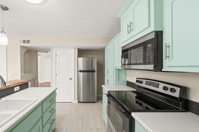 kitchen with pendant lighting, sink, green cabinetry, light tile patterned flooring, and stainless steel appliances