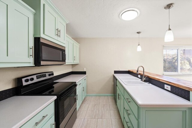 kitchen featuring appliances with stainless steel finishes, sink, light tile patterned floors, green cabinetry, and hanging light fixtures