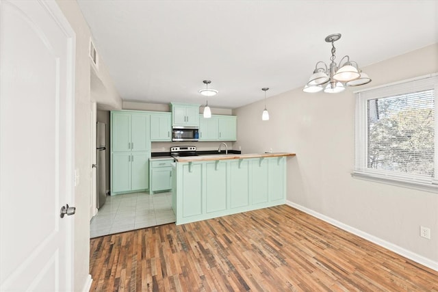 kitchen featuring stainless steel appliances, hardwood / wood-style floors, pendant lighting, a chandelier, and green cabinetry