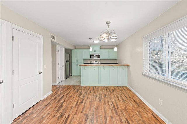 kitchen with appliances with stainless steel finishes, light wood-type flooring, decorative light fixtures, green cabinetry, and a chandelier