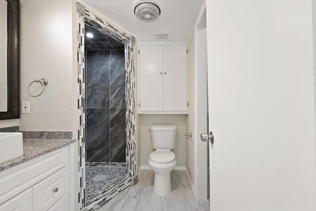 bathroom featuring a tile shower, vanity, and toilet