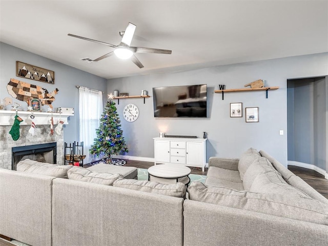 living room featuring dark hardwood / wood-style floors, a stone fireplace, and ceiling fan