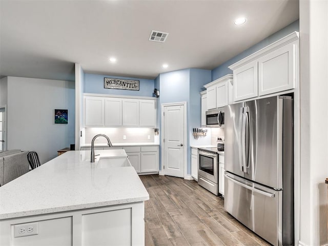 kitchen featuring appliances with stainless steel finishes, light stone counters, sink, white cabinetry, and an island with sink