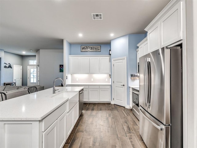 kitchen featuring light stone countertops, stainless steel appliances, dark hardwood / wood-style floors, white cabinetry, and an island with sink