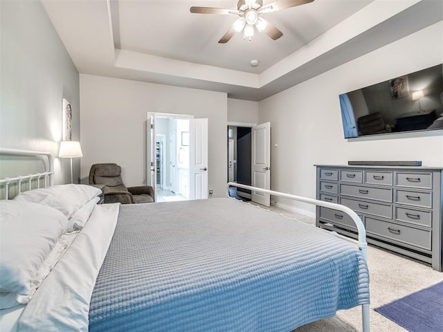 bedroom featuring a raised ceiling, ensuite bath, ceiling fan, and light colored carpet