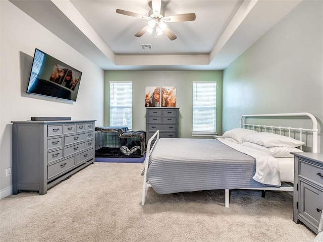 bedroom with a raised ceiling, ceiling fan, and light colored carpet