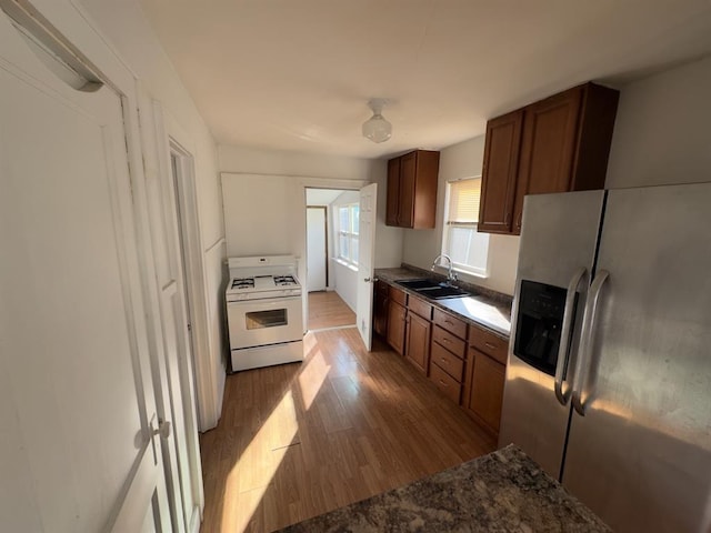 kitchen featuring stainless steel fridge with ice dispenser, sink, light hardwood / wood-style floors, and white gas range oven