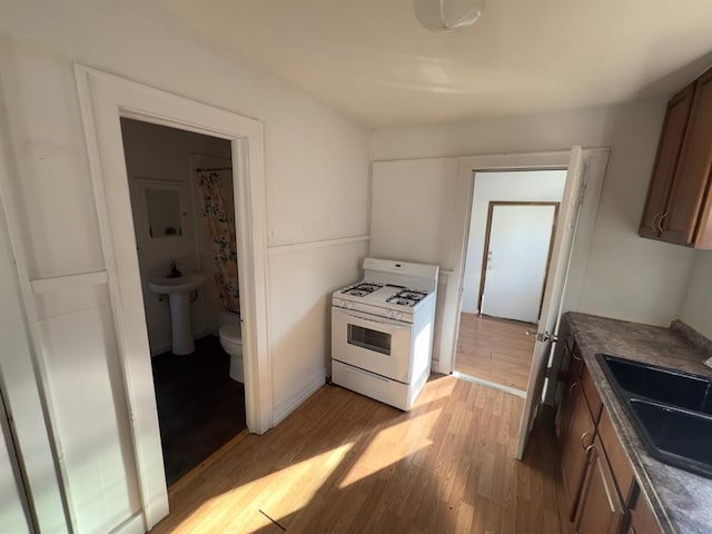 kitchen with white gas range oven, light hardwood / wood-style flooring, and sink