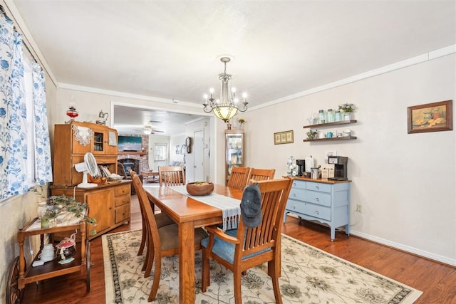 dining space featuring ceiling fan with notable chandelier, hardwood / wood-style flooring, a brick fireplace, and crown molding