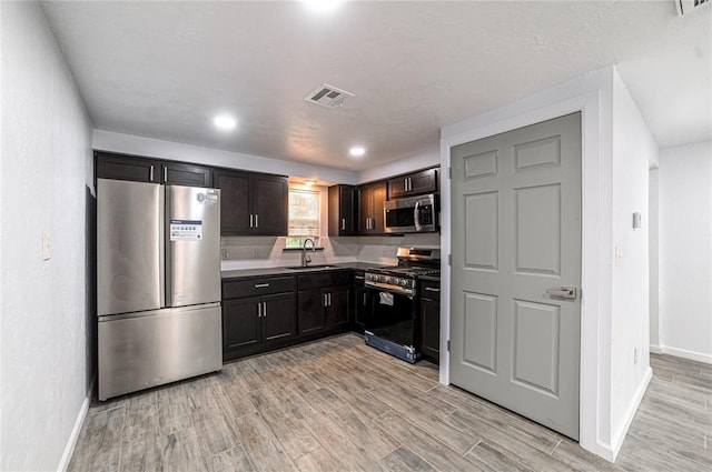 kitchen with appliances with stainless steel finishes, light hardwood / wood-style floors, dark brown cabinets, and sink