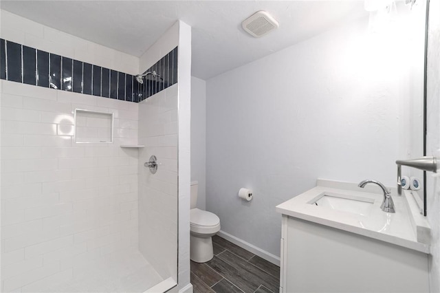 bathroom with a tile shower, vanity, and toilet