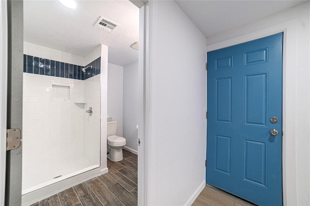 bathroom with tiled shower, wood-type flooring, and toilet