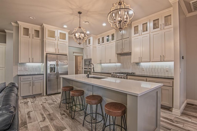 kitchen with hanging light fixtures, a kitchen island with sink, sink, and stainless steel appliances