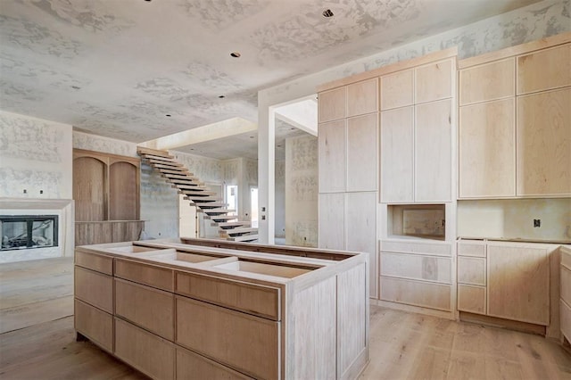 kitchen featuring light brown cabinetry, light wood-type flooring, and a glass covered fireplace