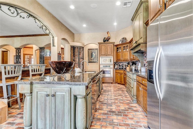 kitchen with appliances with stainless steel finishes, sink, dark stone counters, and an island with sink