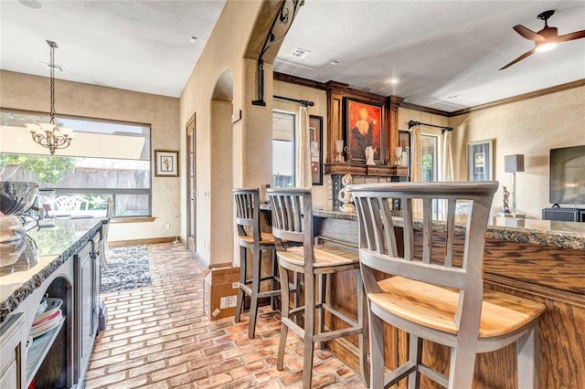 kitchen featuring light stone counters, crown molding, pendant lighting, and ceiling fan with notable chandelier