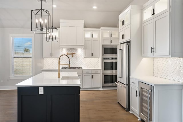 kitchen with white cabinetry, hanging light fixtures, beverage cooler, an island with sink, and appliances with stainless steel finishes