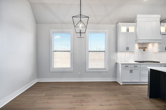 kitchen with pendant lighting, stainless steel gas stovetop, white cabinets, vaulted ceiling, and dark hardwood / wood-style flooring