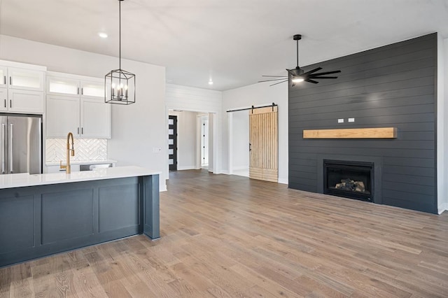 kitchen with stainless steel fridge, light wood-type flooring, a barn door, white cabinetry, and hanging light fixtures