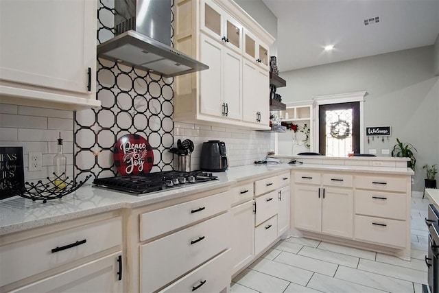 kitchen with white cabinets, backsplash, stainless steel gas cooktop, and wall chimney range hood