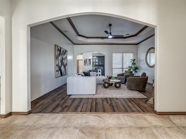 living room featuring ceiling fan with notable chandelier, a raised ceiling, light wood-type flooring, and crown molding