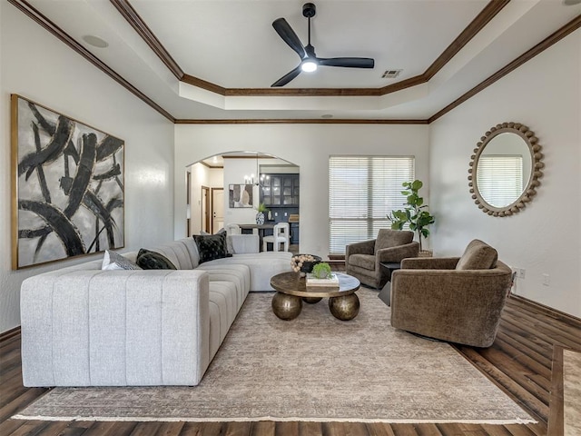 living room with hardwood / wood-style floors, ceiling fan with notable chandelier, a raised ceiling, and ornamental molding