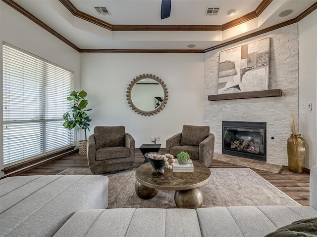 living room with wood-type flooring, a tray ceiling, a stone fireplace, and crown molding