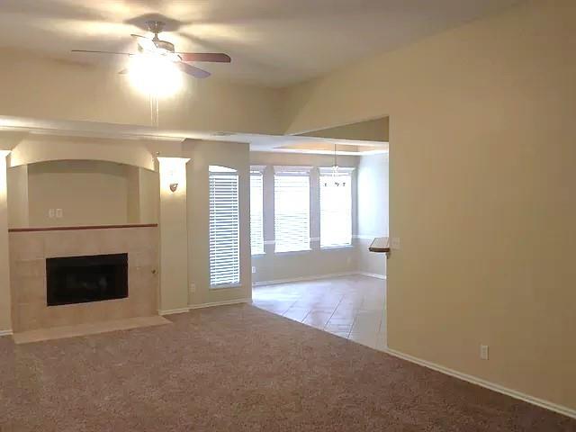 unfurnished living room with carpet, a tile fireplace, and ceiling fan