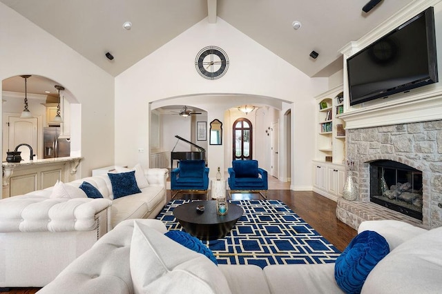 living room featuring beam ceiling, ceiling fan, dark hardwood / wood-style flooring, built in features, and a fireplace