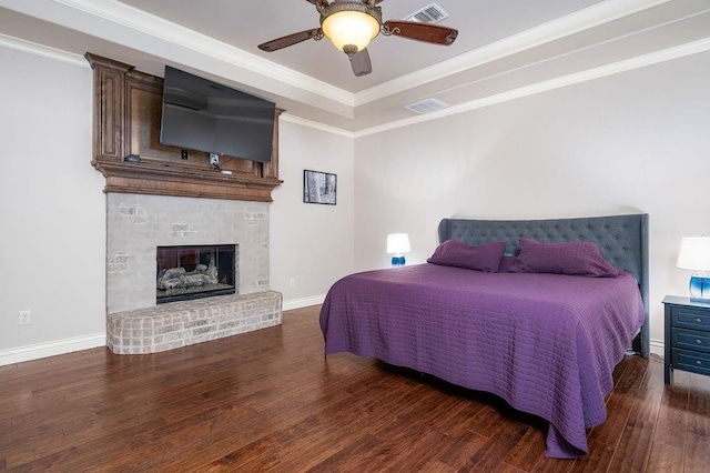 bedroom with dark hardwood / wood-style floors, ceiling fan, crown molding, and a fireplace