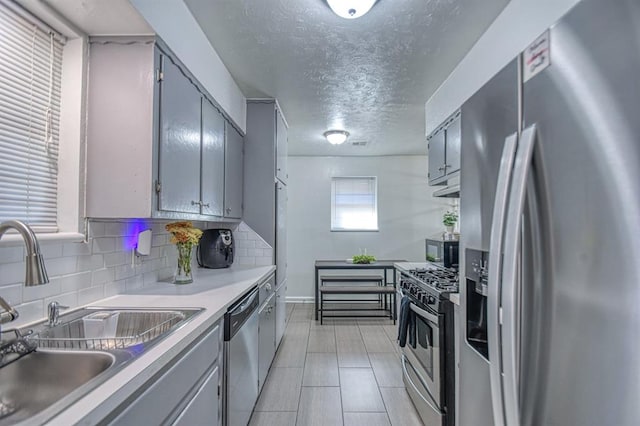 kitchen with sink, stainless steel appliances, tasteful backsplash, a textured ceiling, and gray cabinets